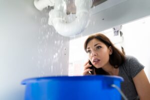 woman-on-cell-phone-looking-at-leak-under-sink